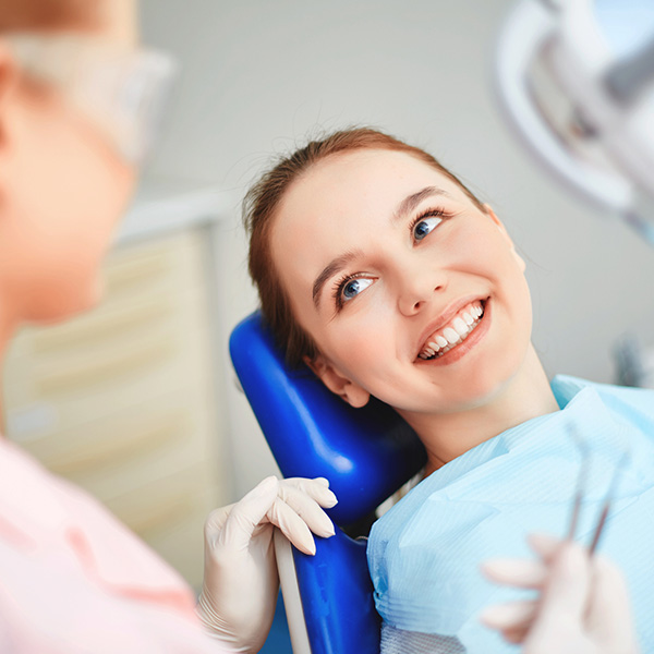 Young female sitting in dentist office and looking at her doctor with smile