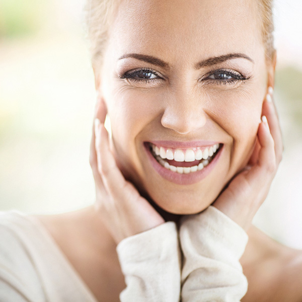 portrait of an attractive mid 30's woman gently touching her neck and smiling while